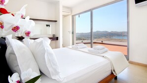 Une chambre d’hôtel avec un lit, du linge de lit blanc, une grande fenêtre donnant sur le paysage et un téléviseur à écran plat fixé au mur.