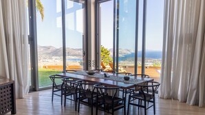 Un espace repas avec une longue table et des chaises, de grandes fenêtres donnant sur un paysage.
