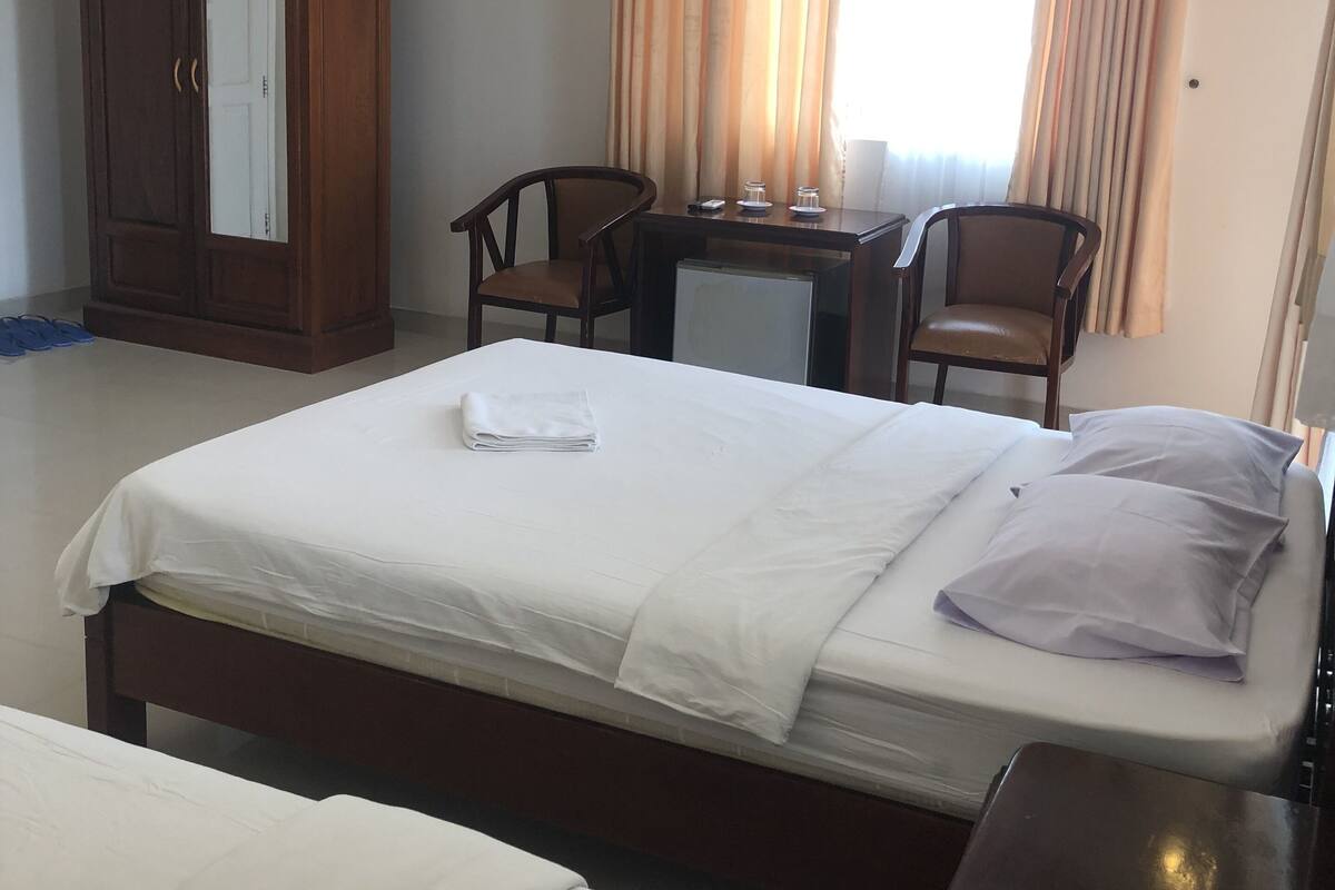 Une chambre d’hôtel avec un grand lit, un bureau, deux chaises, une armoire et un ventilateur de plafond.