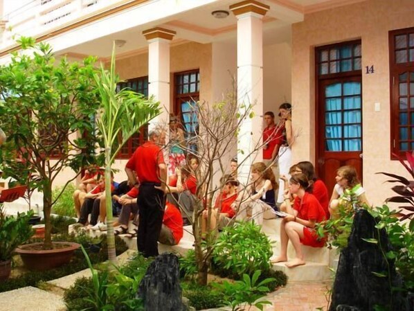 Une cour avec une fontaine, des plantes en pot, et des gens assis et debout.