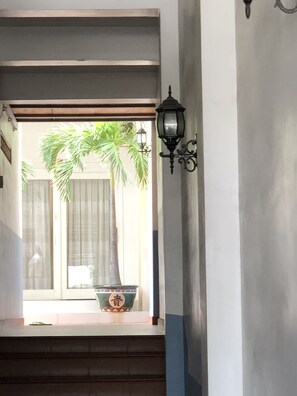 A hallway with a potted plant, a wall-mounted light fixture, and a window with curtains. - Hoang Kim Golden Resort (Mui Ne)