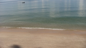 Una playa con agua cristalina, un barco a lo lejos e huellas en la arena.