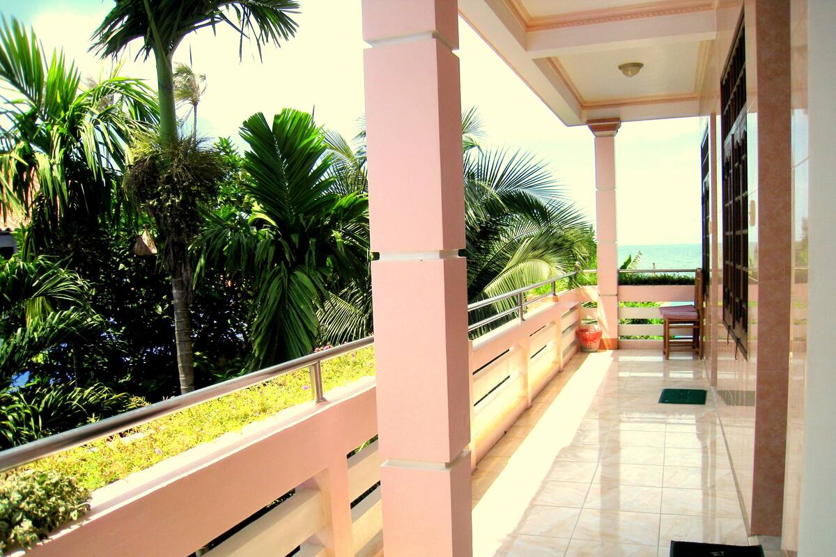 Un balcon abrité offrant une vue sur la mer, entouré d’une végétation luxuriante et doté d’un sol carrelé.