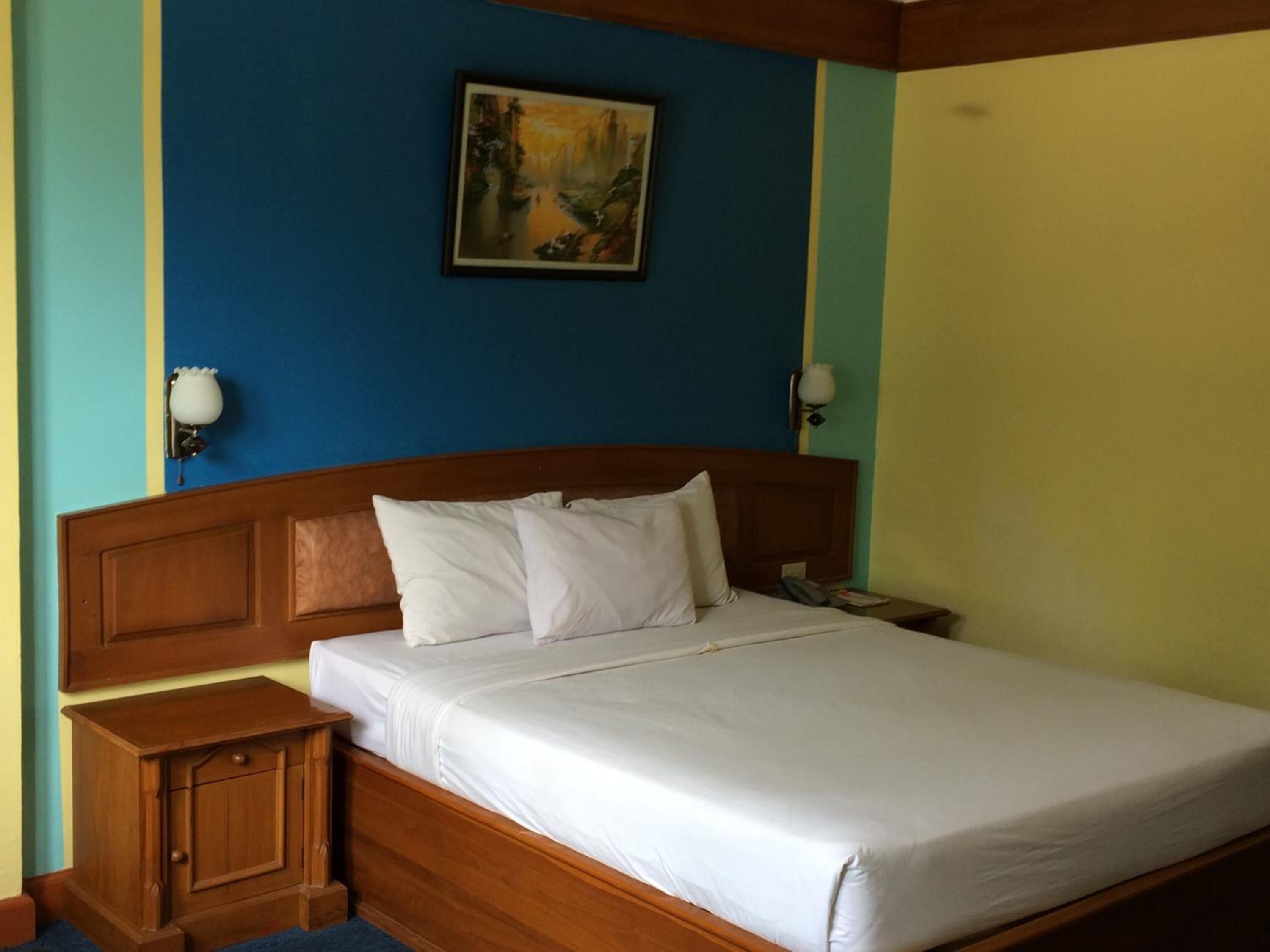 Un dormitorio con cabecera de madera, ropa de cama blanca, una mesita de noche con lámpara y un cuadro en la pared.