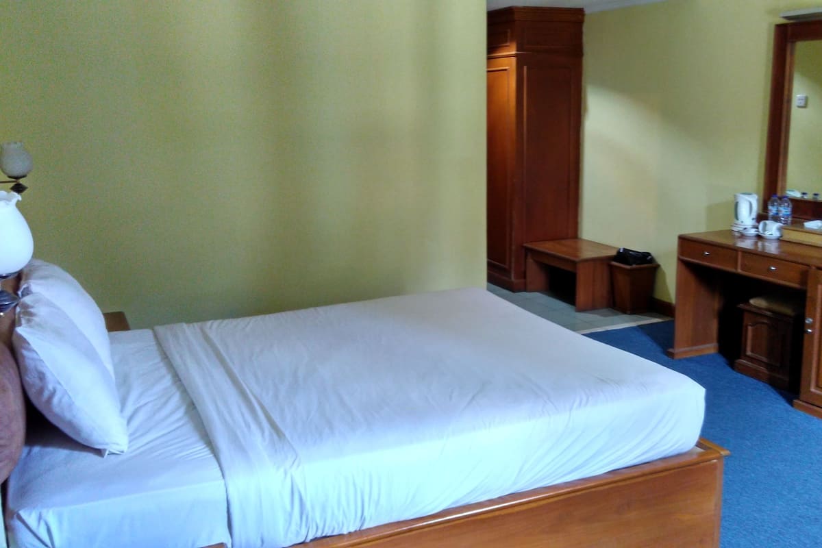 Une chambre d’hôtel comprenant un lit, un bureau, une chaise, une armoire, un miroir, une télévision et une lampe.