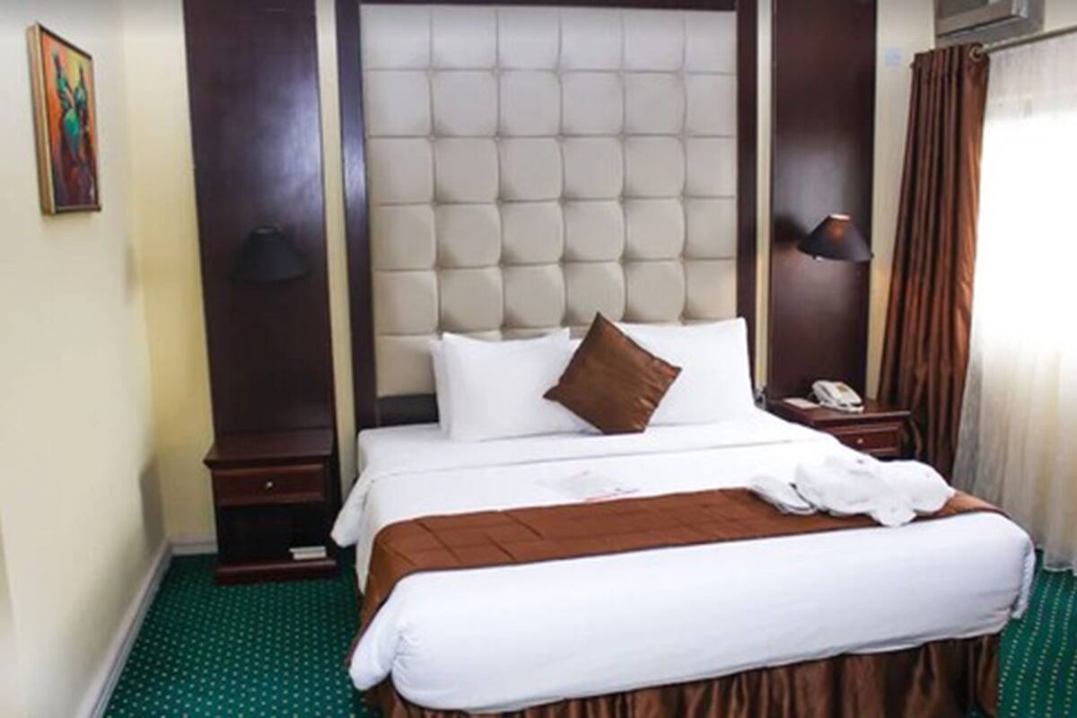 A hotel room with a large bed, a headboard, a bedside table, a lamp, and a curtain.
