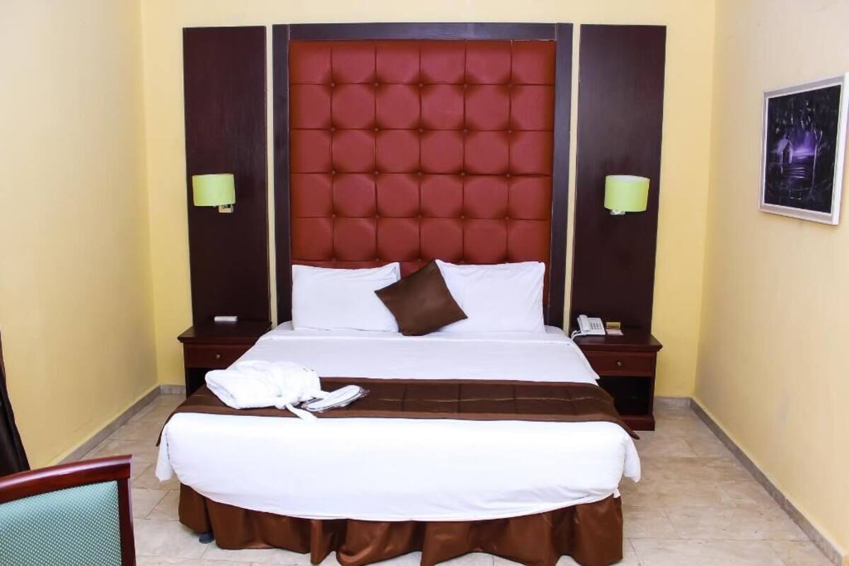 A hotel room with a large bed, two bedside tables, a chair, and a wall-mounted lamp.