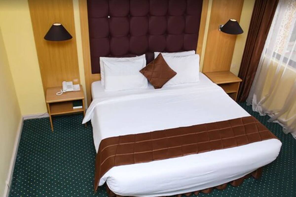 A hotel room with a large bed, two bedside tables, a telephone, and a lamp on each side.
