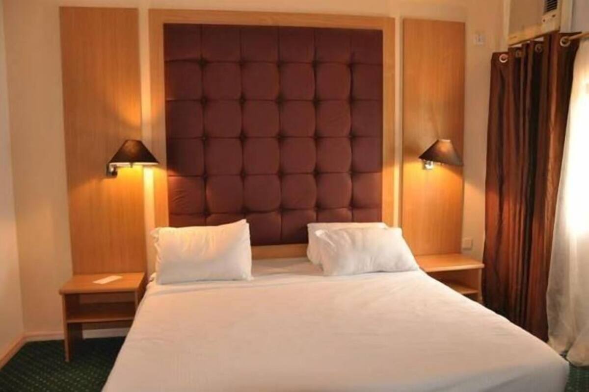 A hotel room with a large tufted headboard, two bedside tables with lamps, and a bed with white bedding.