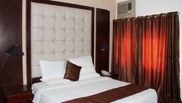 Una habitación de hotel con una cama grande, un cabecero, una mesita de noche con lámpara, un teléfono y una cortina.