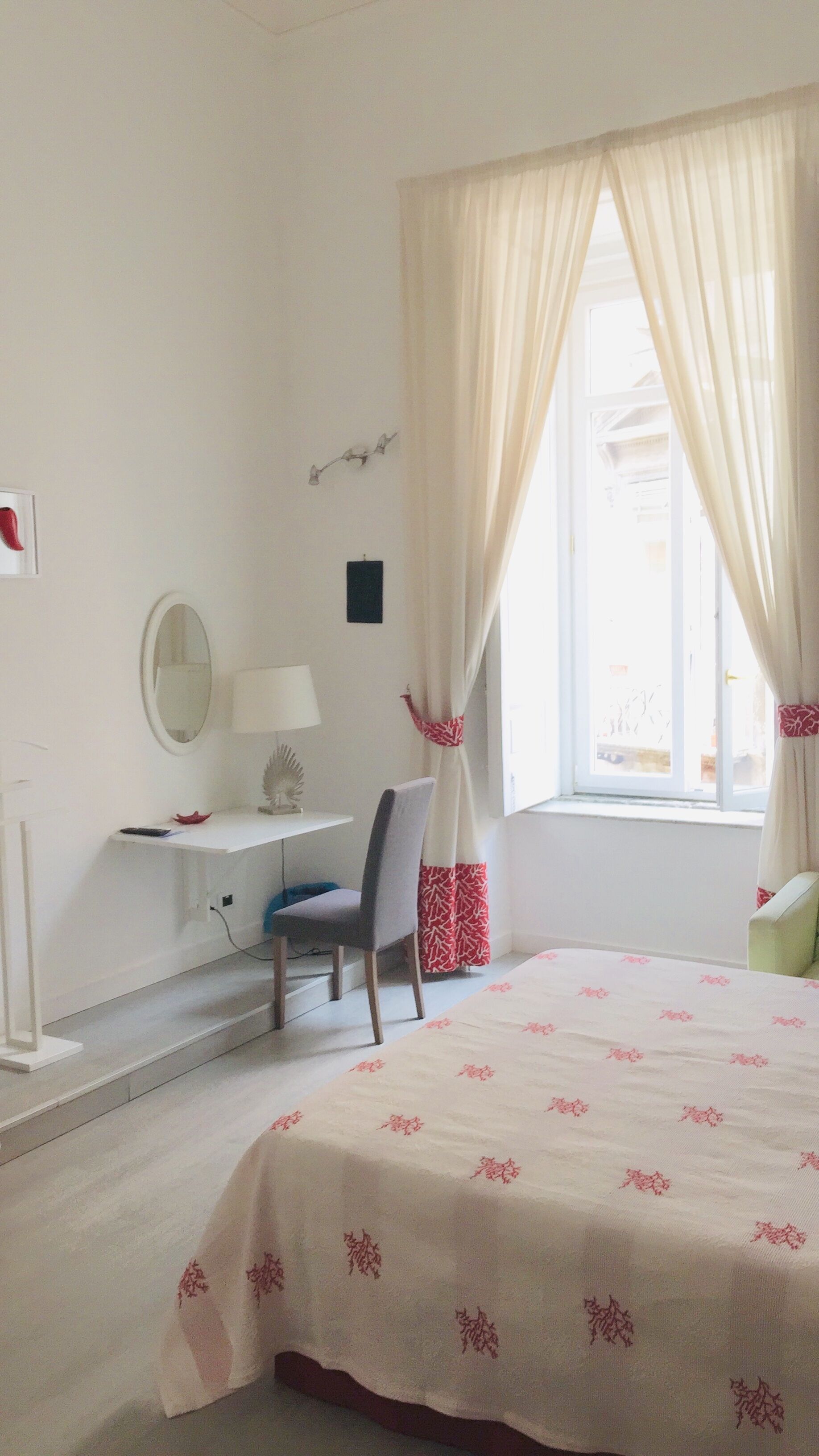 A bedroom with a bed, a desk with a chair, a mirror, and a window with curtains.