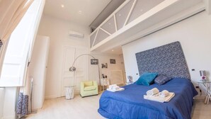 Un dormitorio moderno con una cama grande, un tragaluz, una pequeña zona de estar y una puerta visible.