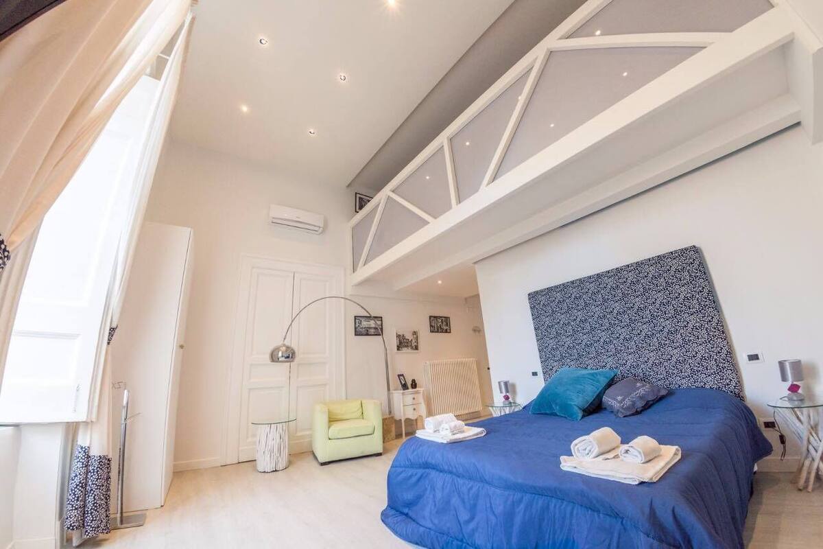 A modern bedroom with a large bed, a skylight, a small seating area, and a visible door.