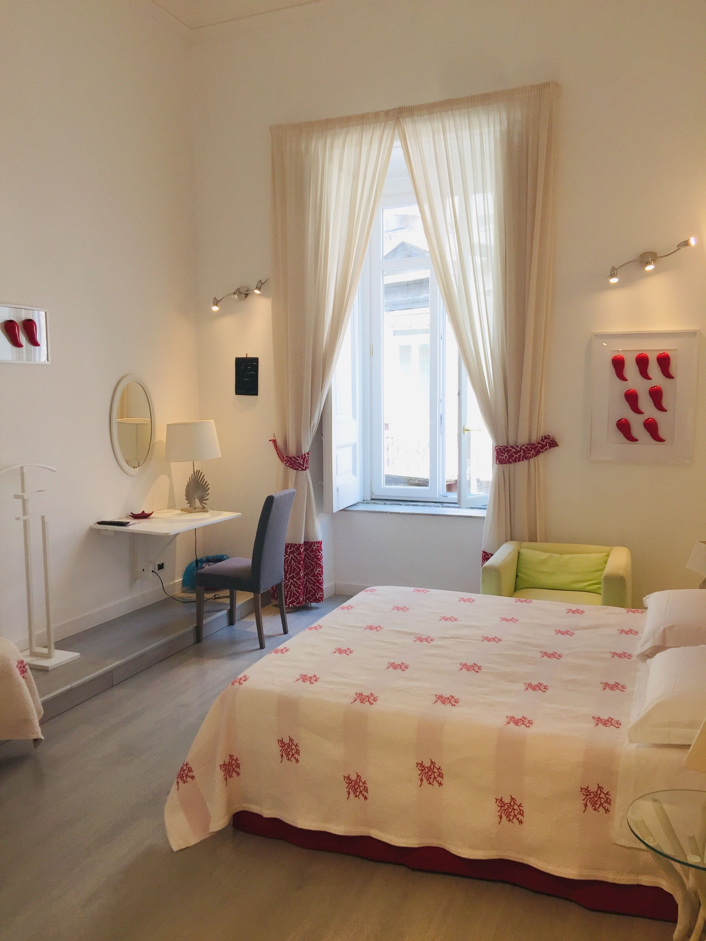 A hotel room with a bed, a desk, a chair, a window with curtains, and a wall with a mirror and artwork.
