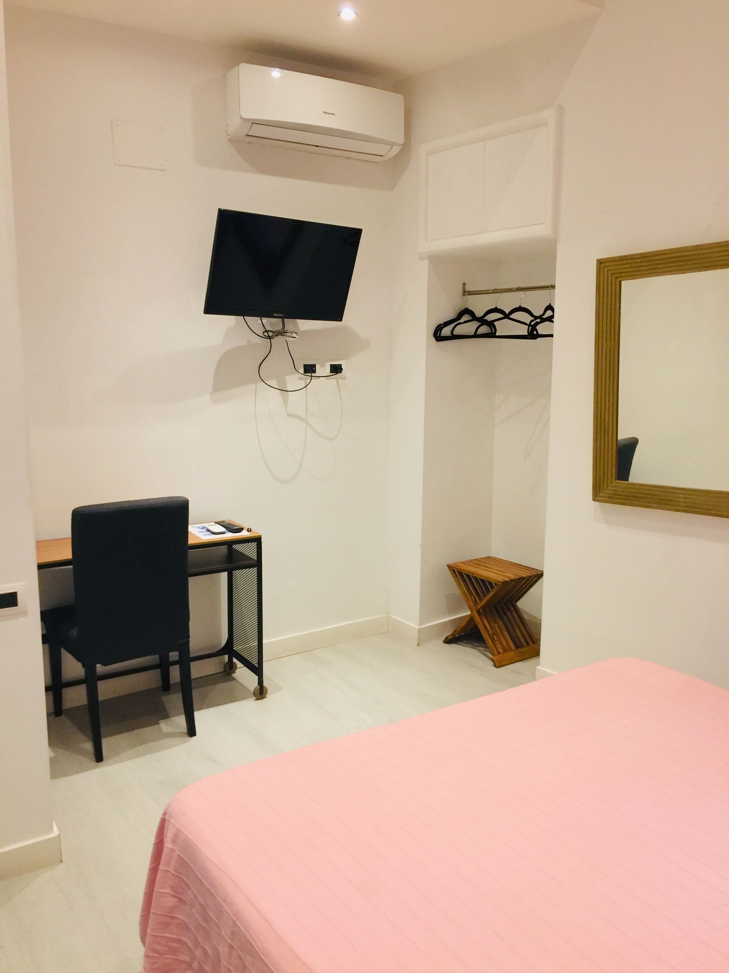 Un dormitorio con cama, escritorio con silla, televisor montado en la pared, armario y espejo.