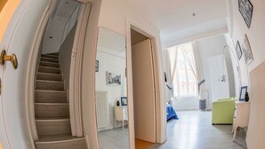 Un pasillo con una escalera que lleva a un dormitorio, una silla verde y un aparador blanco.
