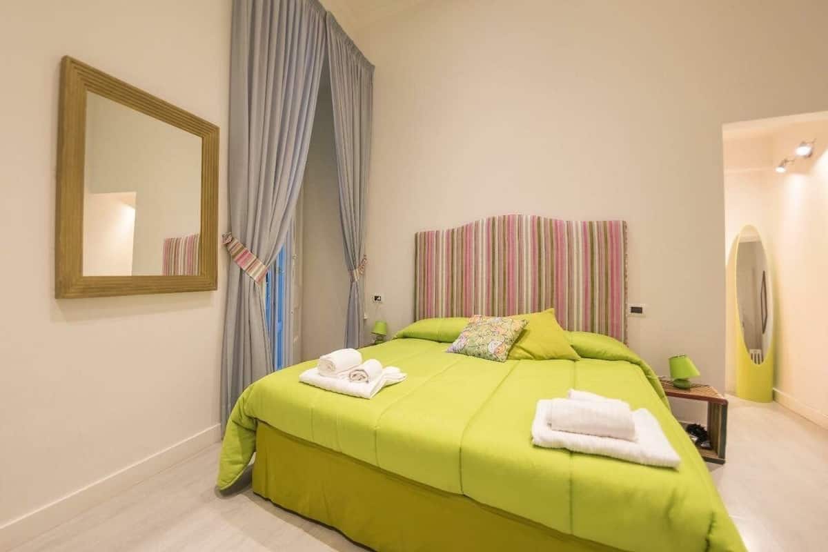 A hotel room with a bed, a mirror, a striped headboard, and a window with curtains.