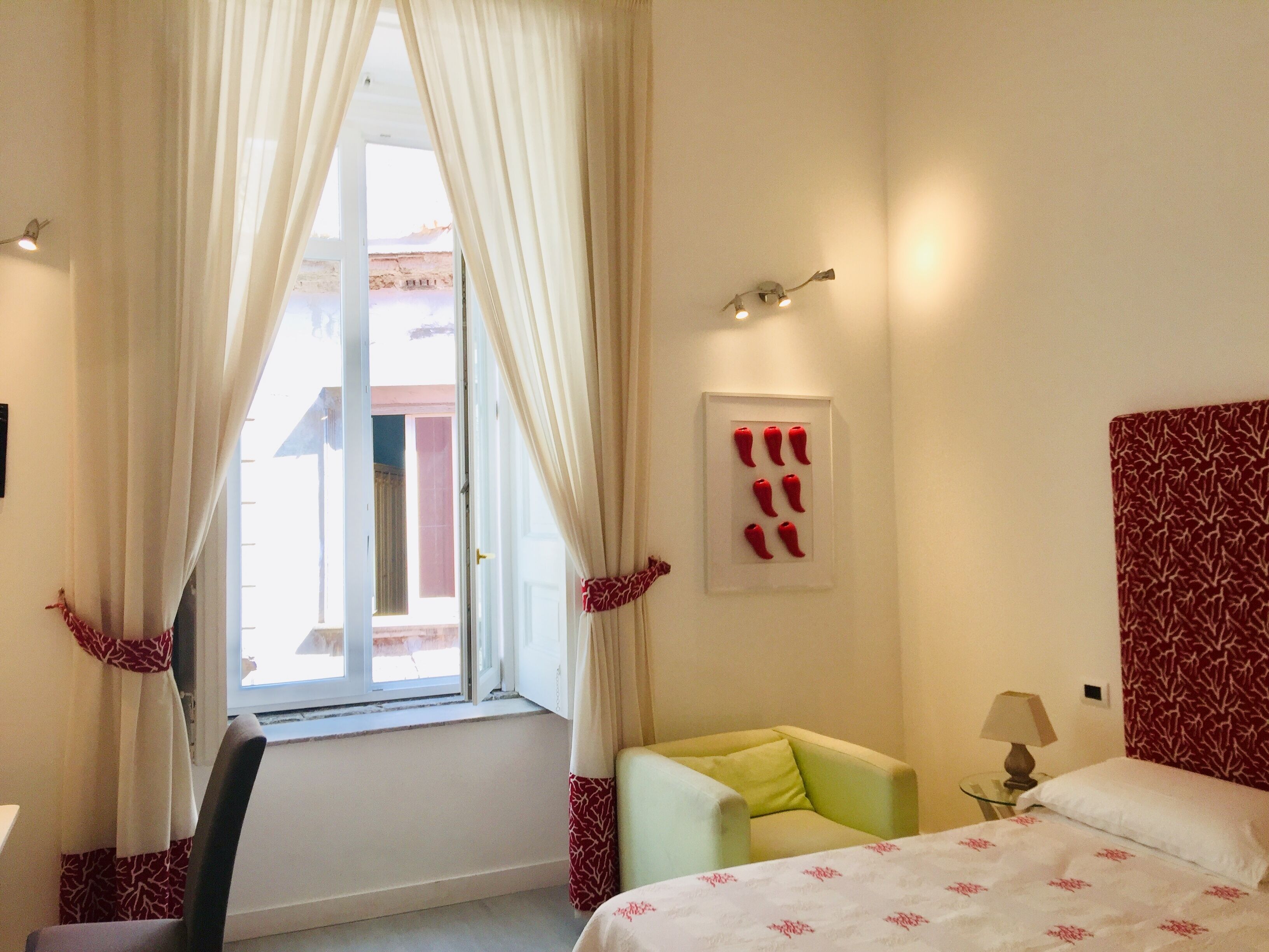 Ein Hotelzimmer mit einem Bett, einem Sessel, einem Tisch mit Lampe, einem Fenster mit Vorhängen und einer Wandleuchte.