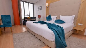 Un dormitorio moderno con una cama grande, una silla azul, un escritorio y una ventana con vistas.