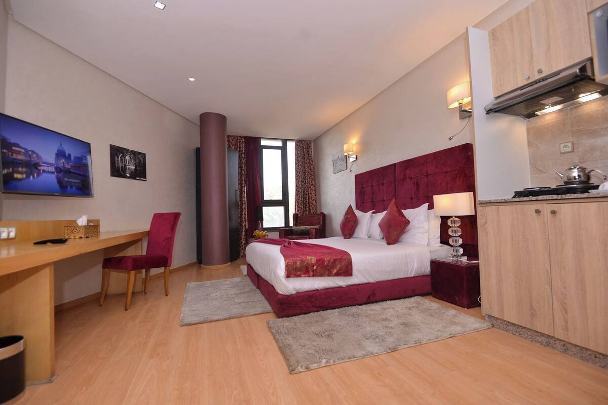 Una habitación de hotel moderna con una cama grande, un escritorio, una silla, un televisor y una kitchenette.