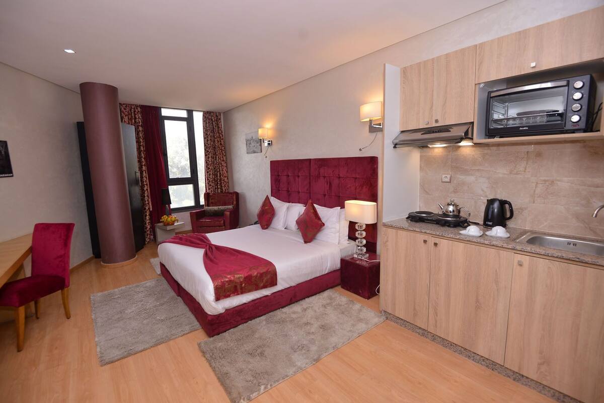 Habitación de hotel con cama, escritorio, silla, cabecero tapizado de color rojo, microondas y lavabo.