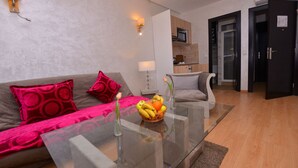 Una sala de estar moderna con una mesa de centro de vidrio, un sofá con cojines rojos, una zona de cocina con microondas y una puerta con un cartel.