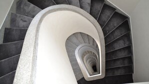 Una escalera de caracol de diseño moderno, con un pilar blanco central y escalones oscuros.