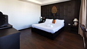 Une chambre d’hôtel moderne dotée d’un grand lit, d’un parquet en bois foncé, d’un téléviseur à écran plat, de deux tables de chevet avec lampes et d’un panneau décoratif mural.