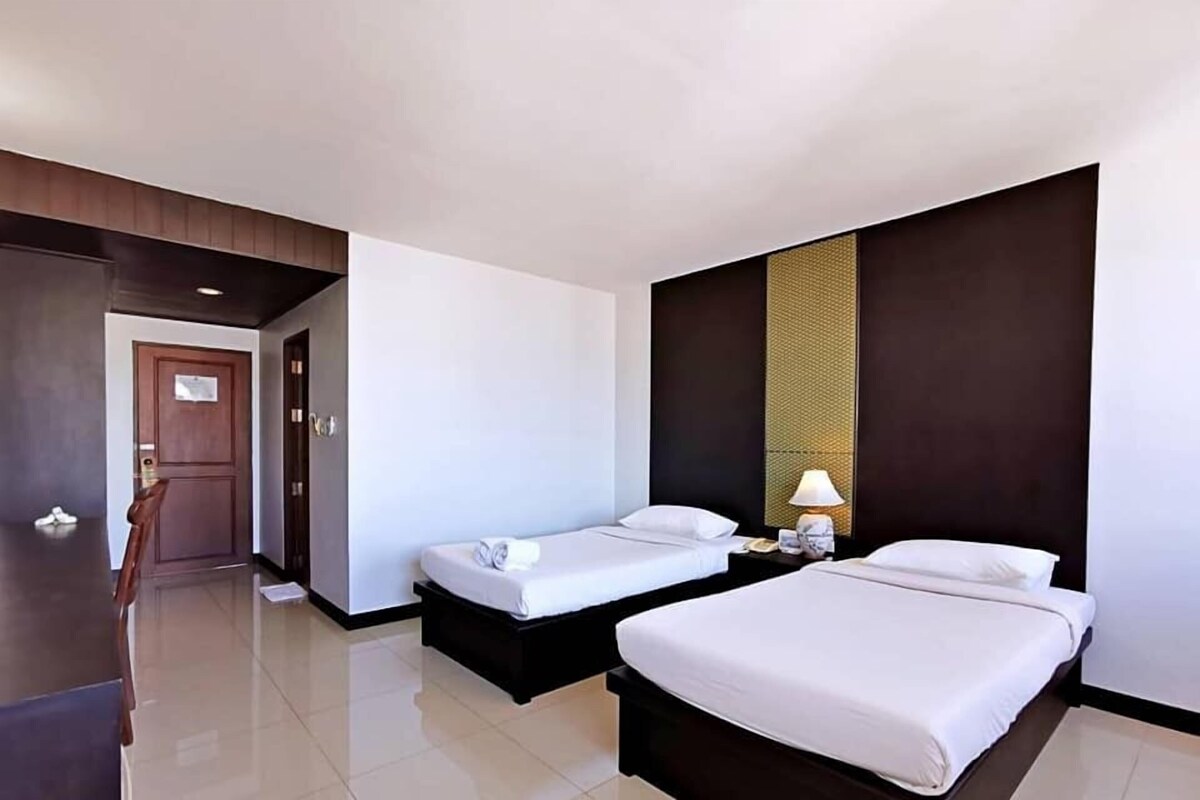 A hotel room with two beds, a door, a nightstand, and a lamp.