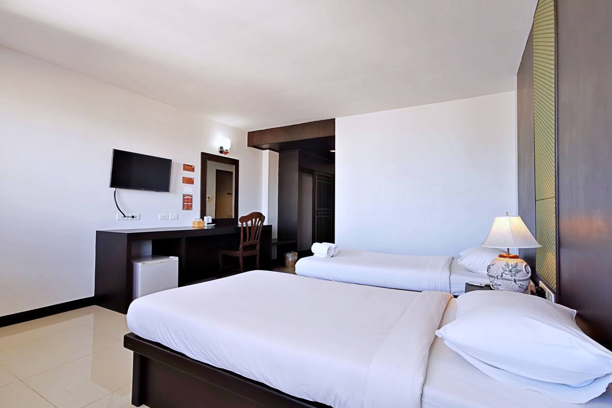 A hotel room with two beds, a desk, a TV, and a lamp.