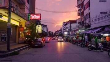 A street scene at dusk with buildings, shops, and parked vehicles.