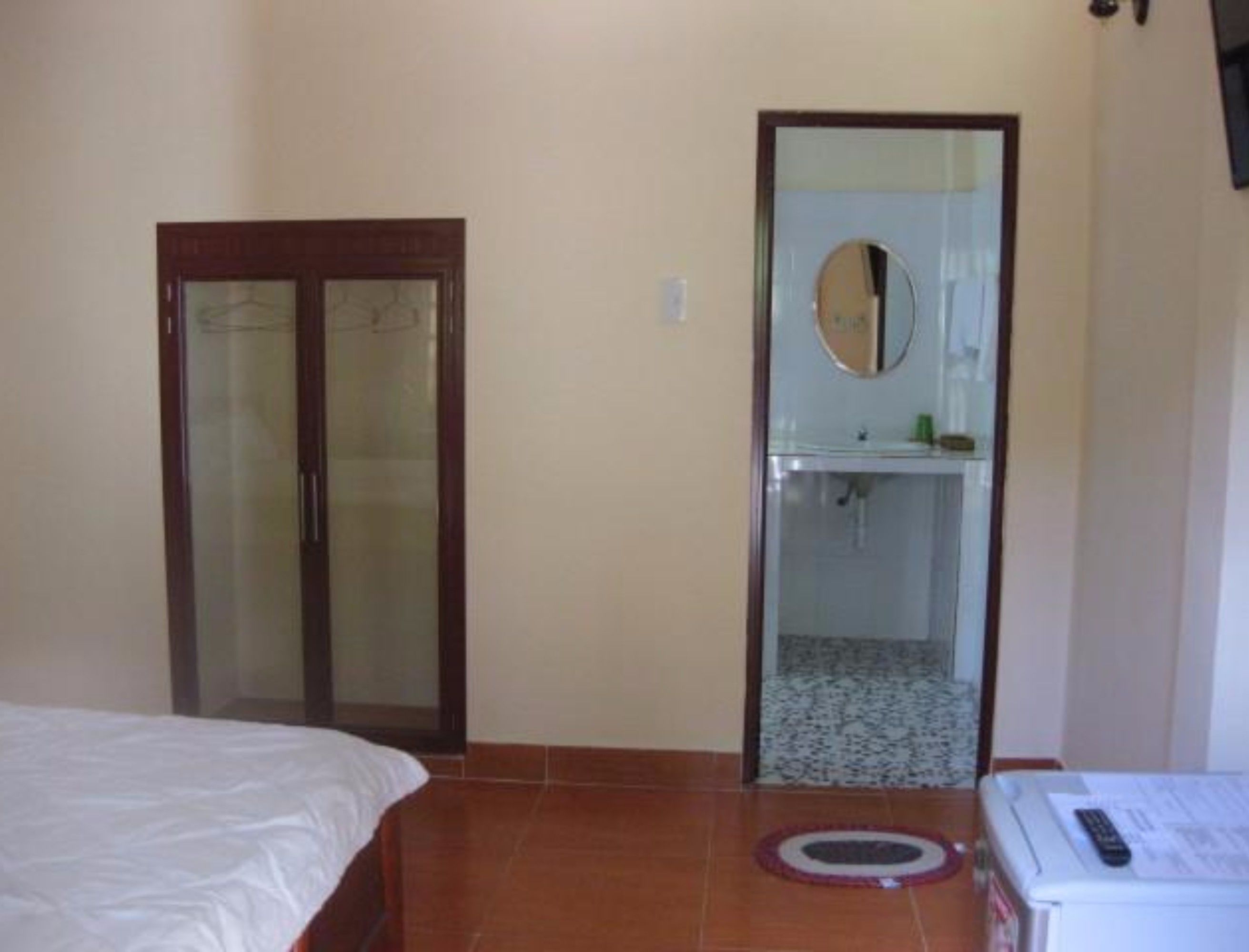 A bedroom with a bed, a door, a bathroom with a mirror, and a tiled floor.