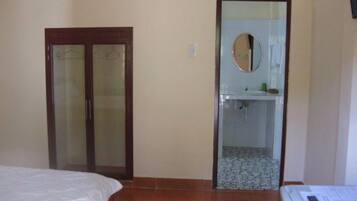 A bedroom with a bed, a door, a bathroom with a mirror, and a tiled floor.