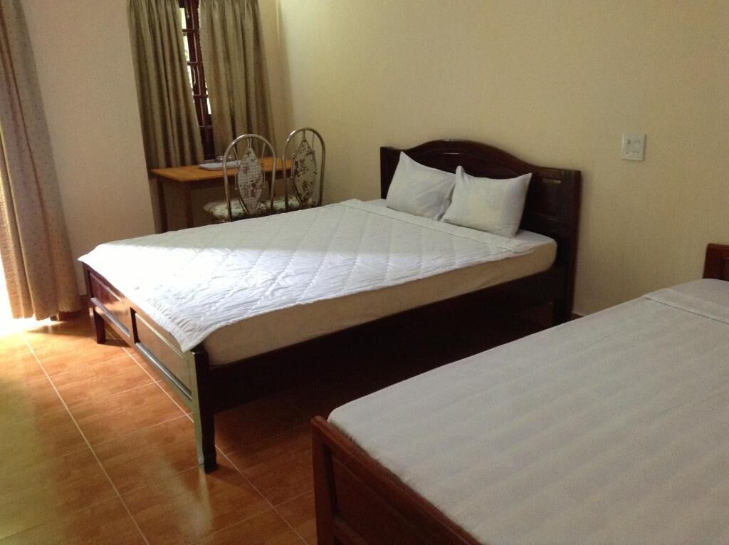 A room with two single beds, a wooden headboard, a small table with a chair, and a window with curtains.
