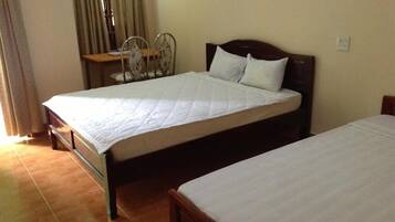 A room with two single beds, a wooden headboard, a small table with a chair, and a window with curtains.