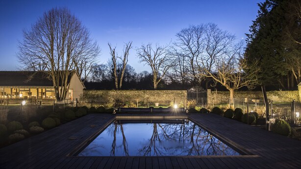 A rectangular swimming pool with a wooden deck, surrounded by trees and a stone wall. - Hôtel de L'Abbaye Le Tronchet - Handwritten Collection (Le Tronchet)