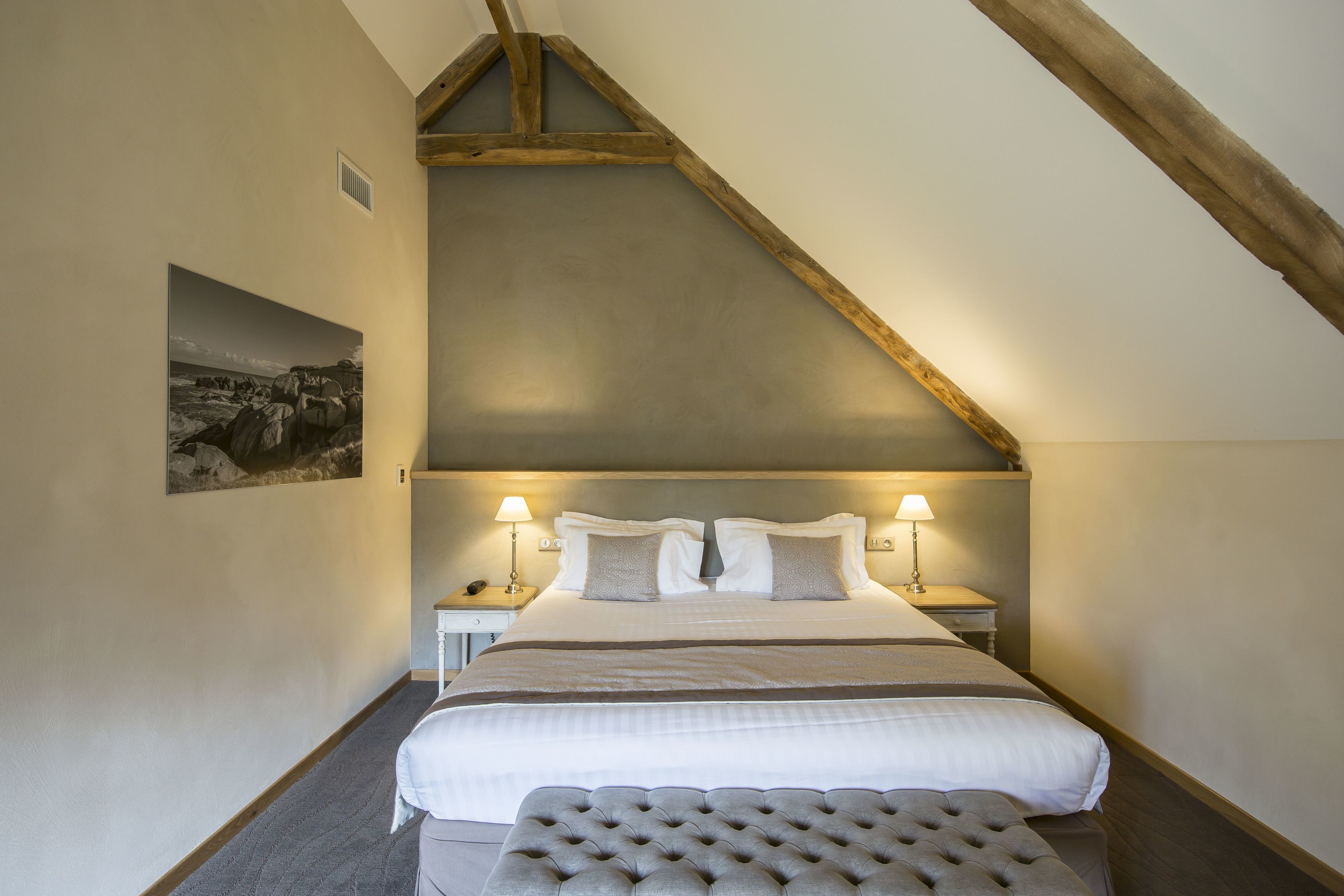 Une chambre à coucher avec un grand lit, deux tables de chevet et une tête de lit ornée de poutres apparentes.