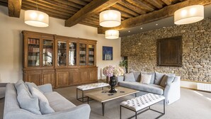 A spacious living room with a stone wall, wooden ceiling beams, and a large bookcase. - Hôtel de L'Abbaye Le Tronchet - Handwritten Collection (Le Tronchet)