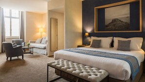 A hotel room with a large bed, a seating area with a chair and a table, a lamp, and a framed picture on the wall. - Hôtel de L'Abbaye Le Tronchet - Handwritten Collection (Le Tronchet)