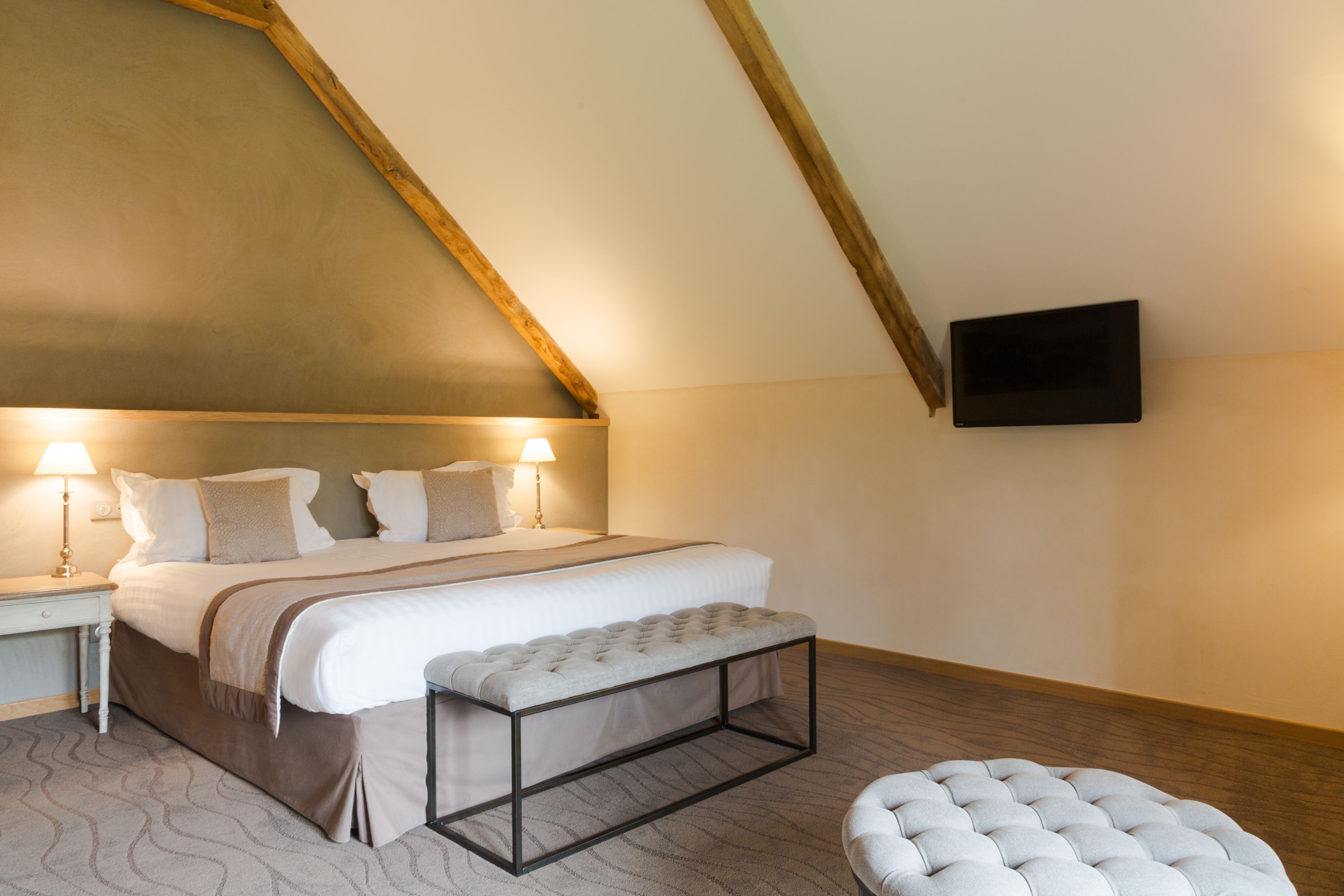 A bedroom with a large bed, bedside lamps, a flat-screen TV, and a wooden ceiling.