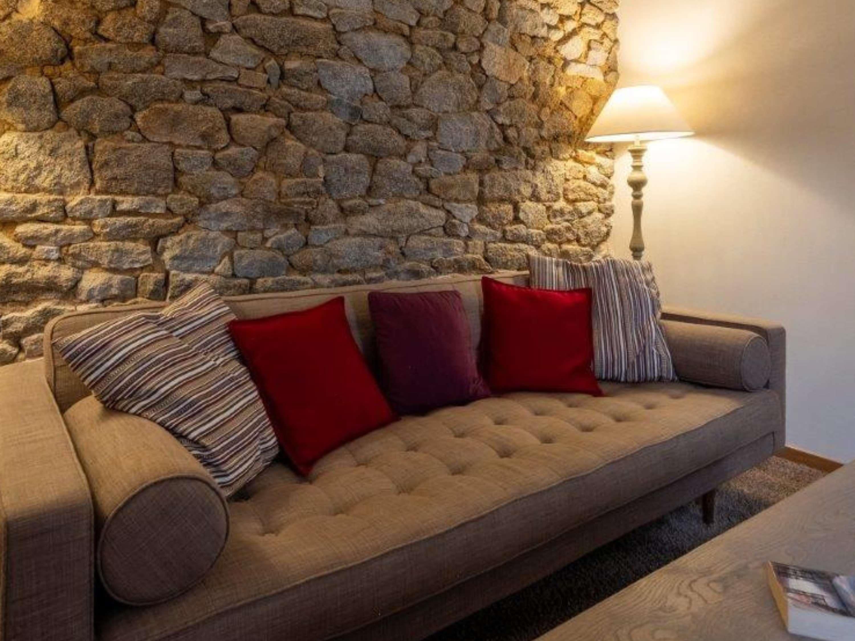 A sofa with a stone wall backdrop, a lamp, and a book on a table.