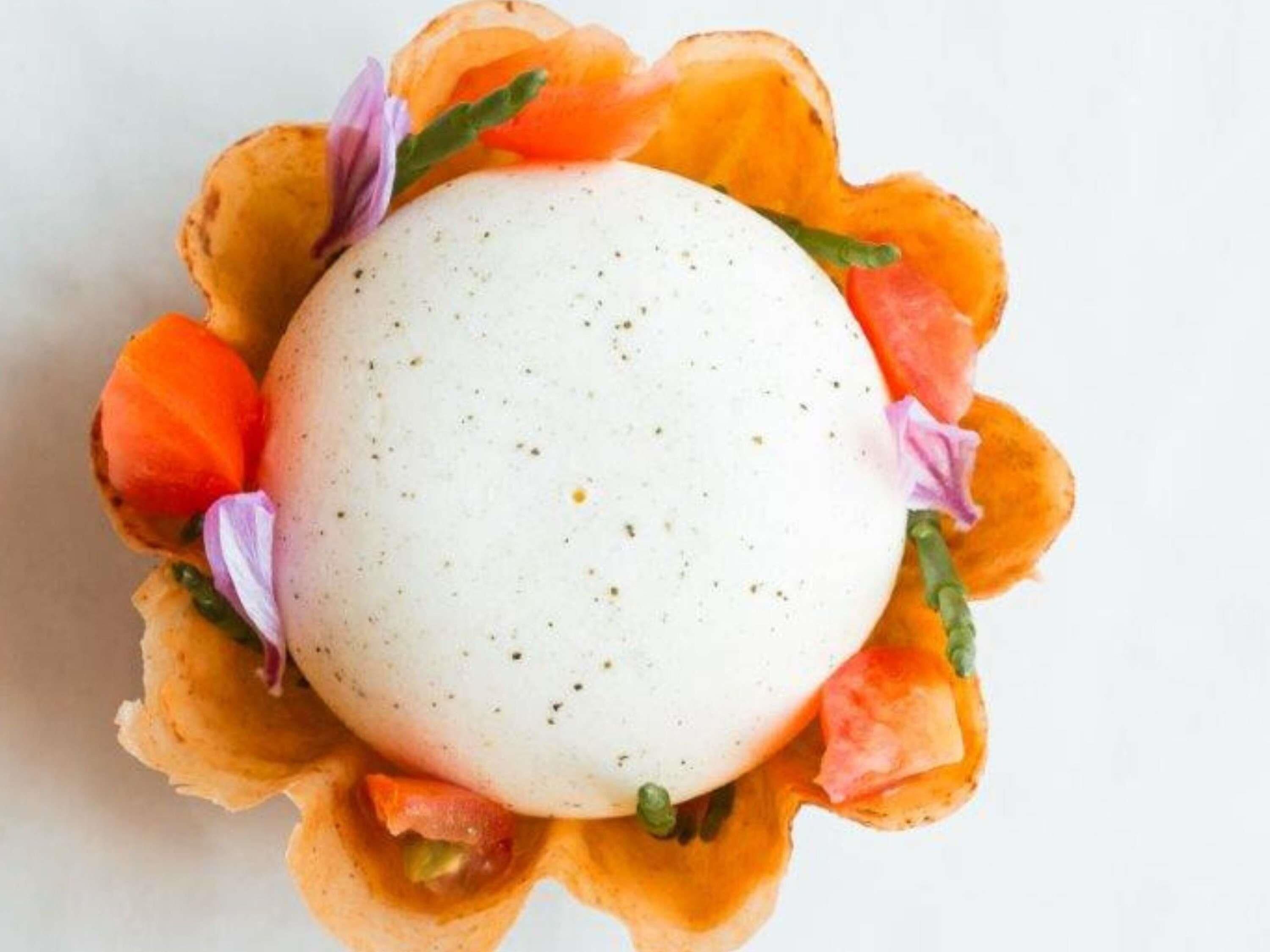 A round white object with specks, surrounded by orange petals and purple flowers.