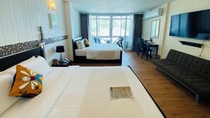 Een hotelkamer met twee bedden, een sofa, een televisie en een balkon met een tafel en stoelen.