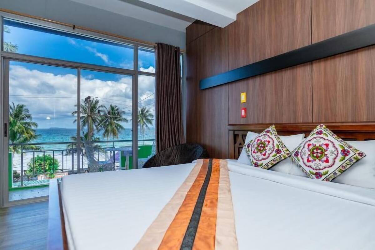 Ein Hotelzimmer mit großem Fenster, einem Bett mit gestreifter Bettdecke und zwei Zierkissen.