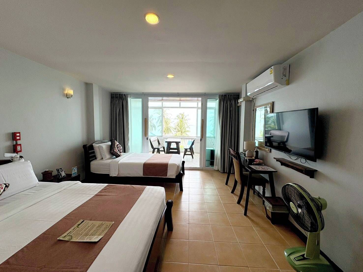 A hotel room with two beds, a TV, a desk with a chair, and a balcony with a view.
