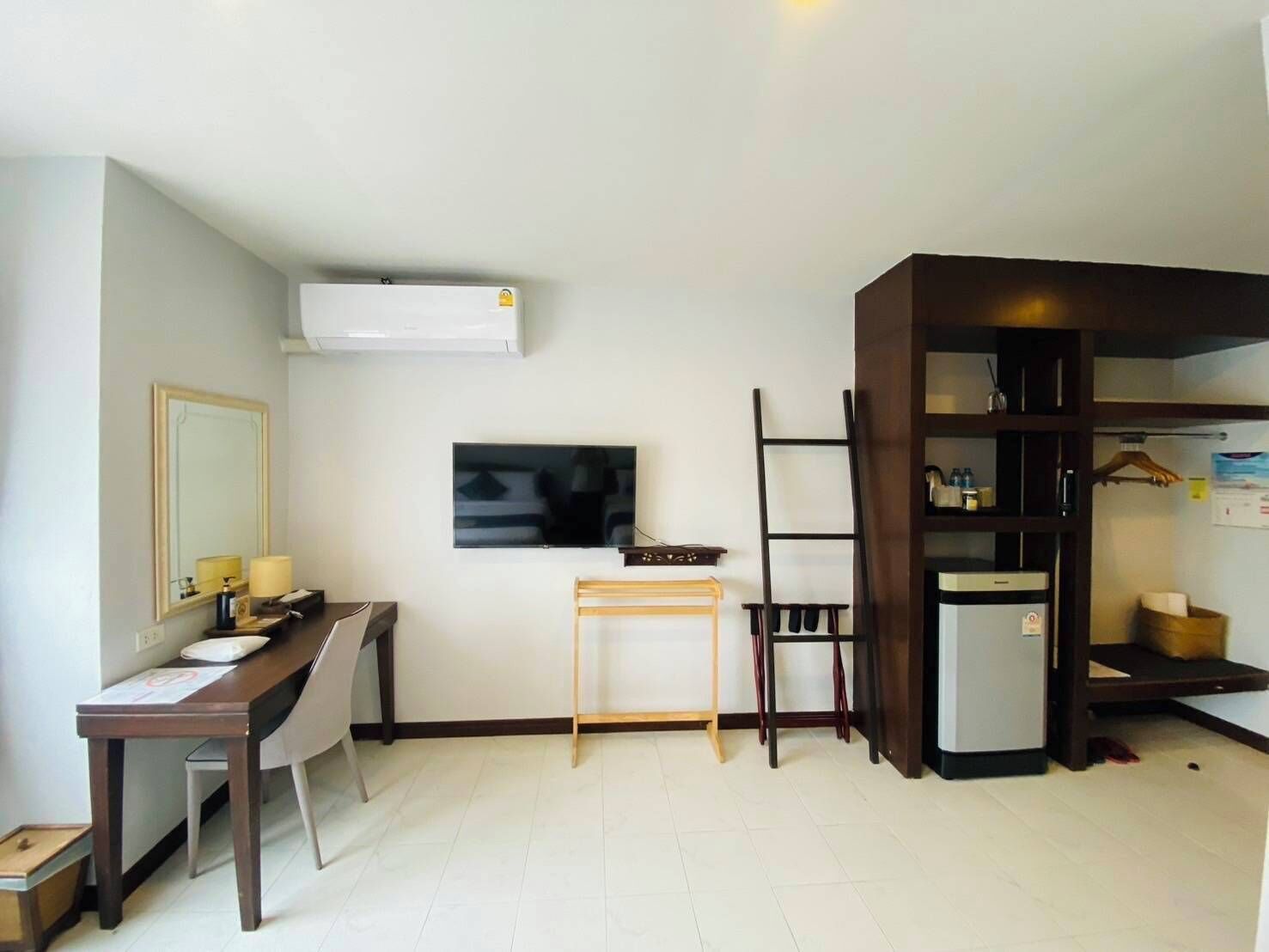 A compact hotel room with a desk, chair, TV, wardrobe, and a small table.