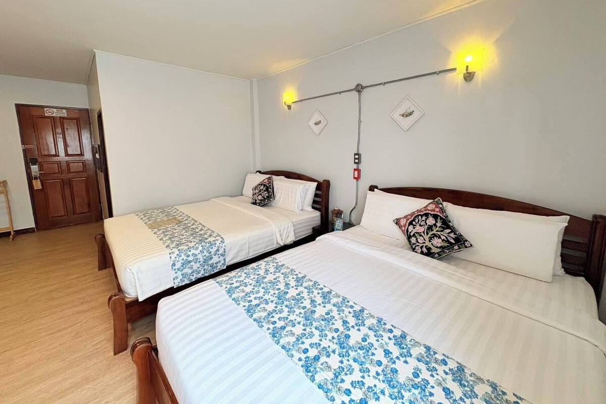 Ein Hotelzimmer mit zwei Einzelbetten, einer Holztür, einem Lichtschalter und einer Wandleuchte.