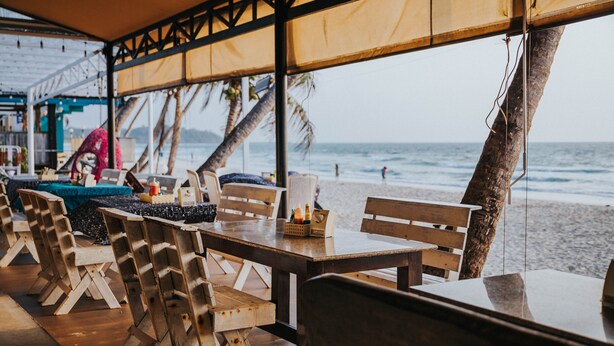 Een restaurant aan het strand met houten meubels en uitzicht op de oceaan.