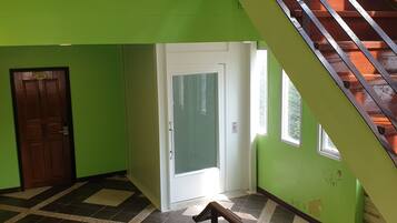 A room with green walls, a wooden door, a white door, a staircase, and a tiled floor.