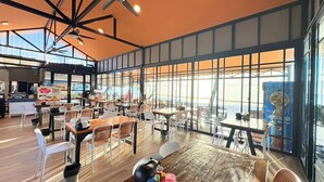 Een restaurant met hoge plafonds, grote ramen en diverse zithoeken.